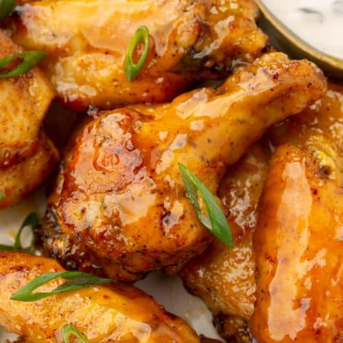 A close up of mango habanero wings on a plate topped with green onions and a ramekin of bleu cheese dressing in the background.