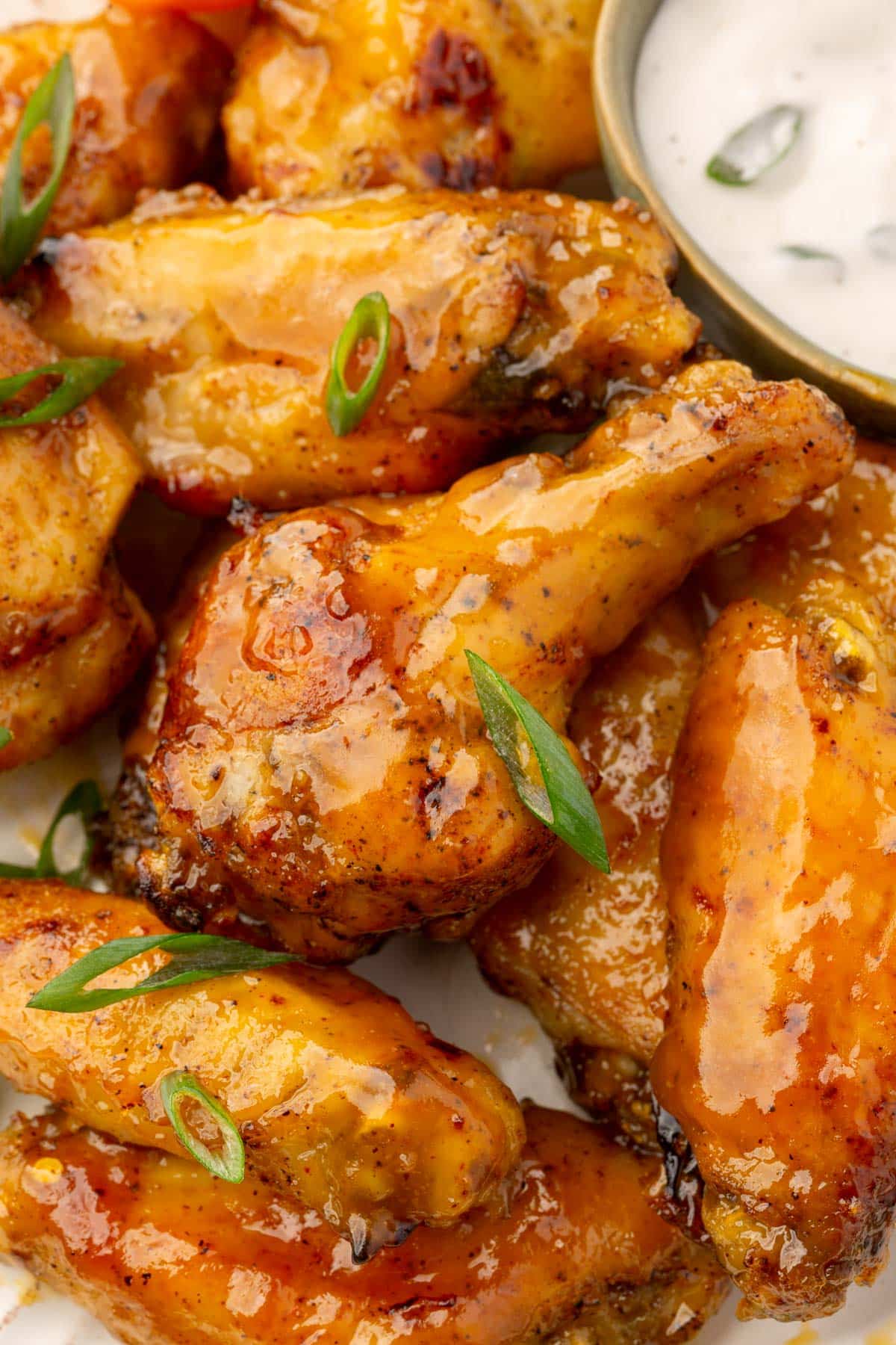 A close up of mango habanero wings on a plate topped with green onions and a ramekin of bleu cheese dressing in the background.