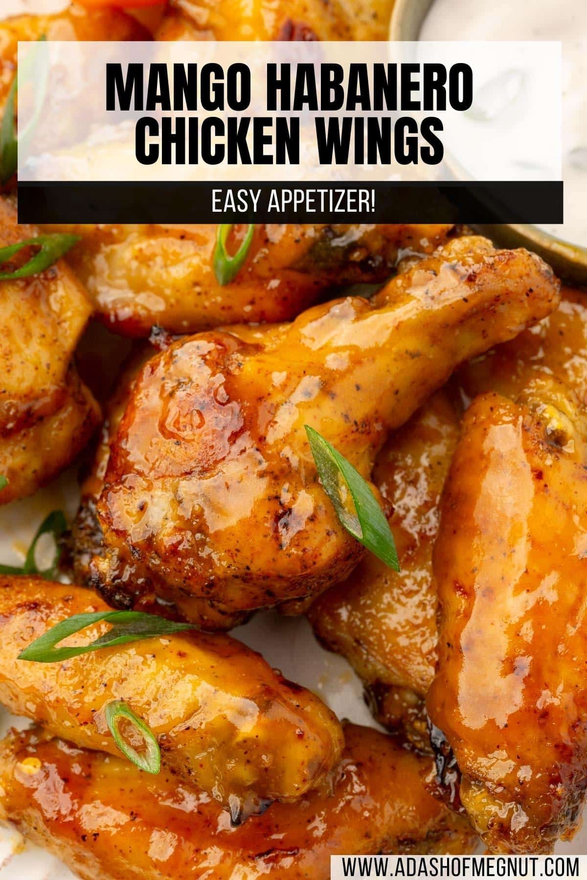 A close up of mango habanero wings on a plate topped with green onions and a ramekin of bleu cheese dressing in the background.