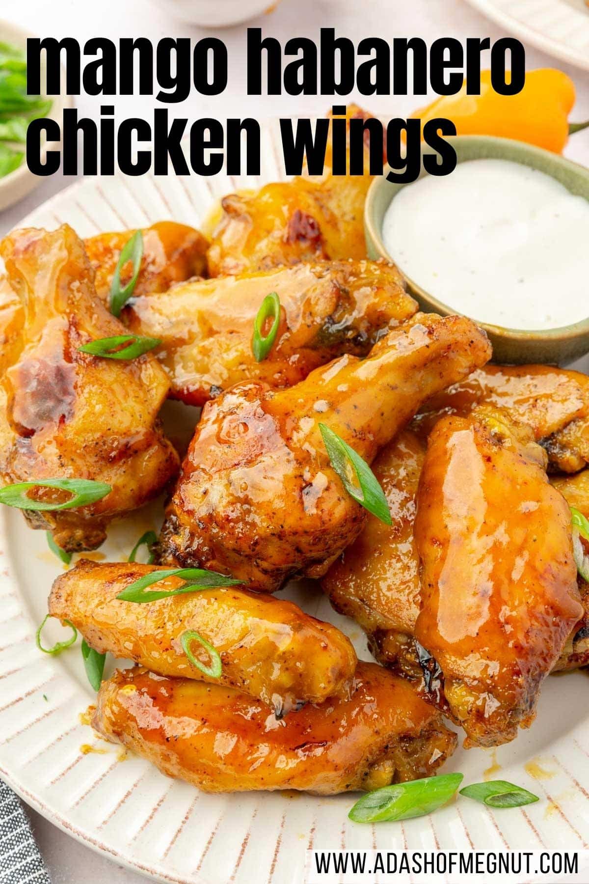 A close up of mango habanero wings with a ramekin of bleu cheese dressing to the side topped with green onions.