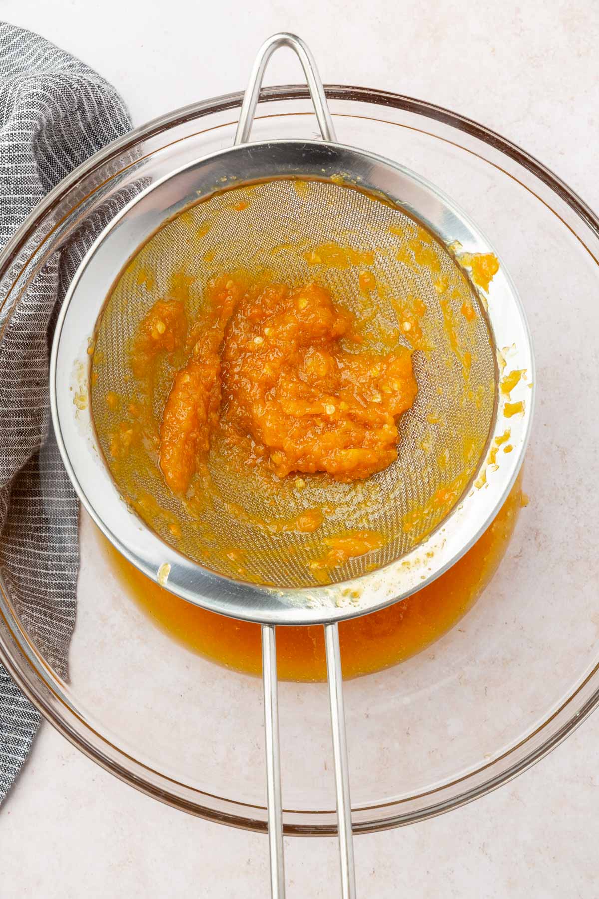 A mine mesh sieve with mango and habanero pulp over a glass mixing bowl.