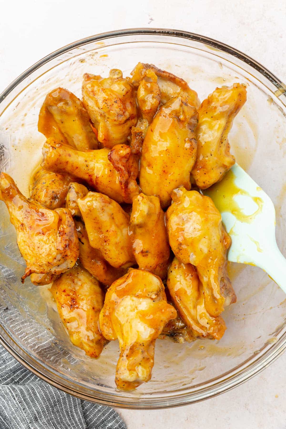 Mango habanero glazed chicken wings in a glass bowl with a rubber spatula.