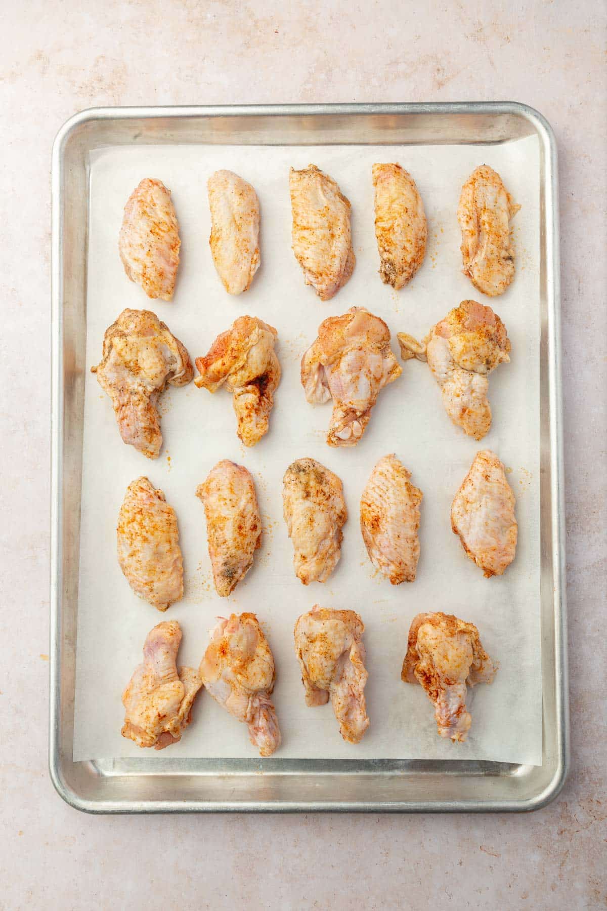 Raw chicken wings tossed in oil and spices on a parchment lined baking sheet.