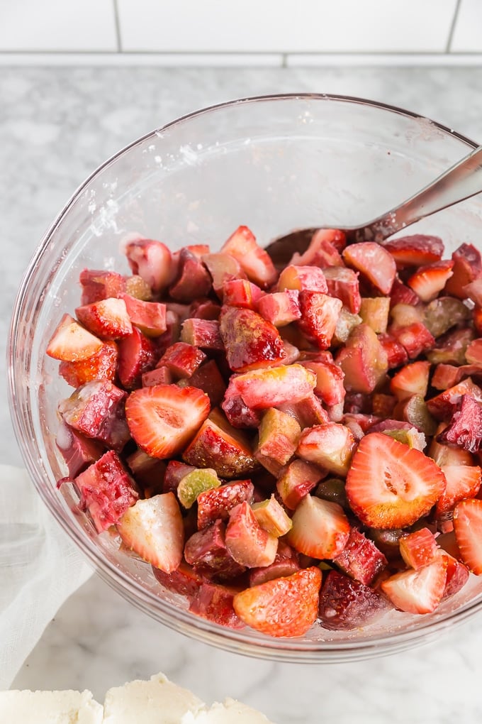 Strawberries and rhubarb in a cornstarch mixture in a glass mixing bowl.