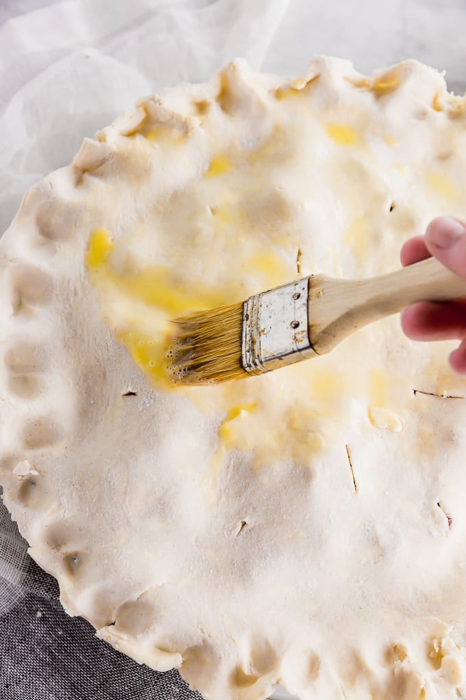 A pastry brush brushing egg wash on a raw gluten-free pie dough crust before baking in the oven.