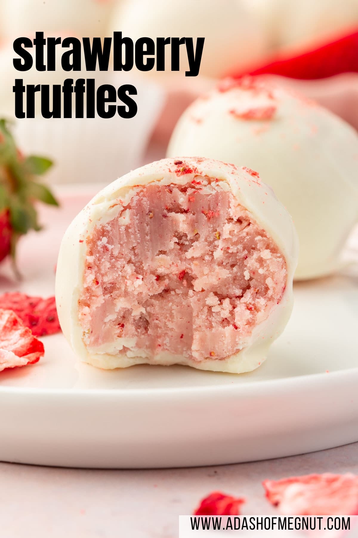 A single white chocolate strawberry truffle on a plate with more truffles in the background.
