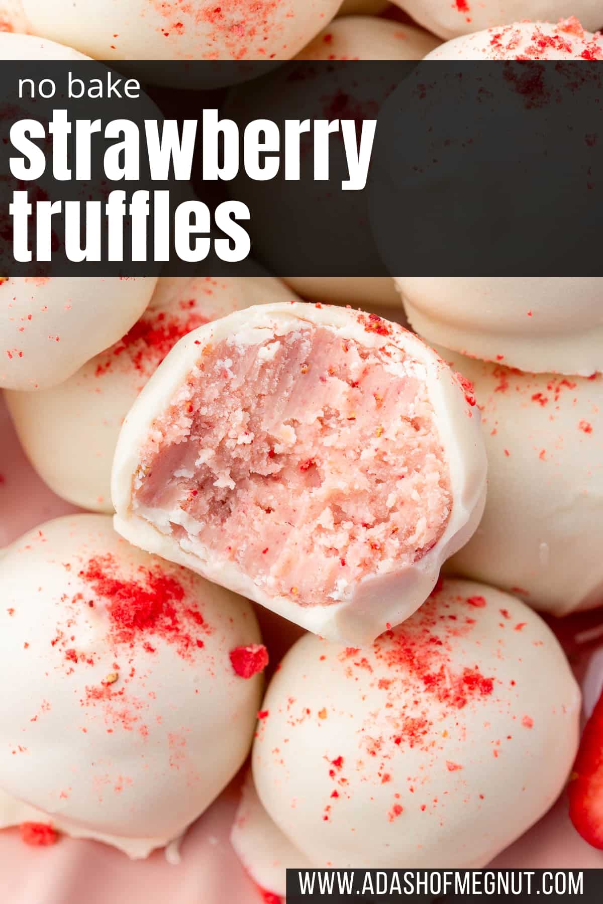 A close up of a strawberry truffle with a bite taken out of it on a pile of more white chocolate strawberry truffles.