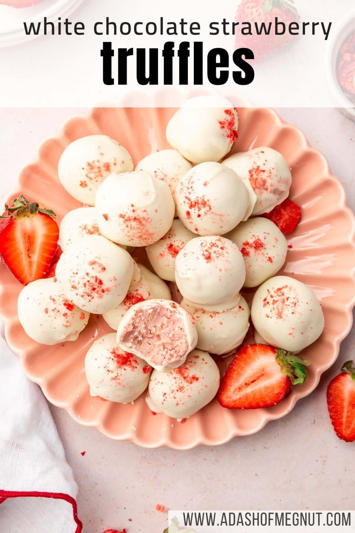 An overhead view of a pink scalloped plate with a pile of white chocolate strawberry truffles and strawberry halves on it.