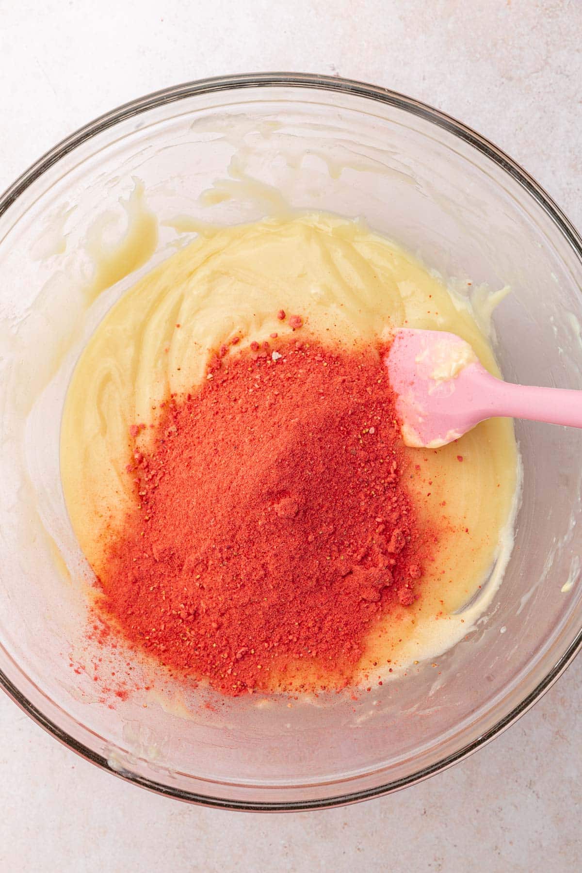 A glass mixing bowl with melted white chocolate topped with freeze-dried strawberry powder.
