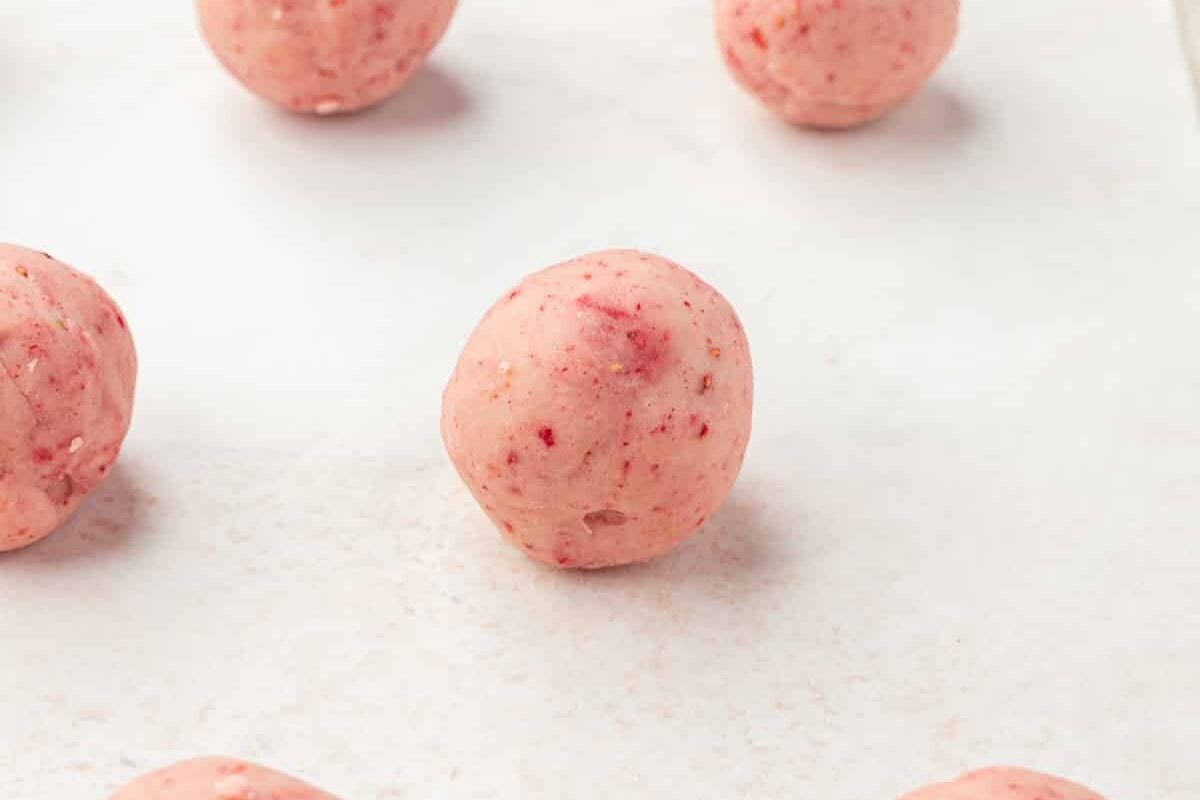 A baking sheet lined with parchment paper with a dozen strawberry truffle balls on it.