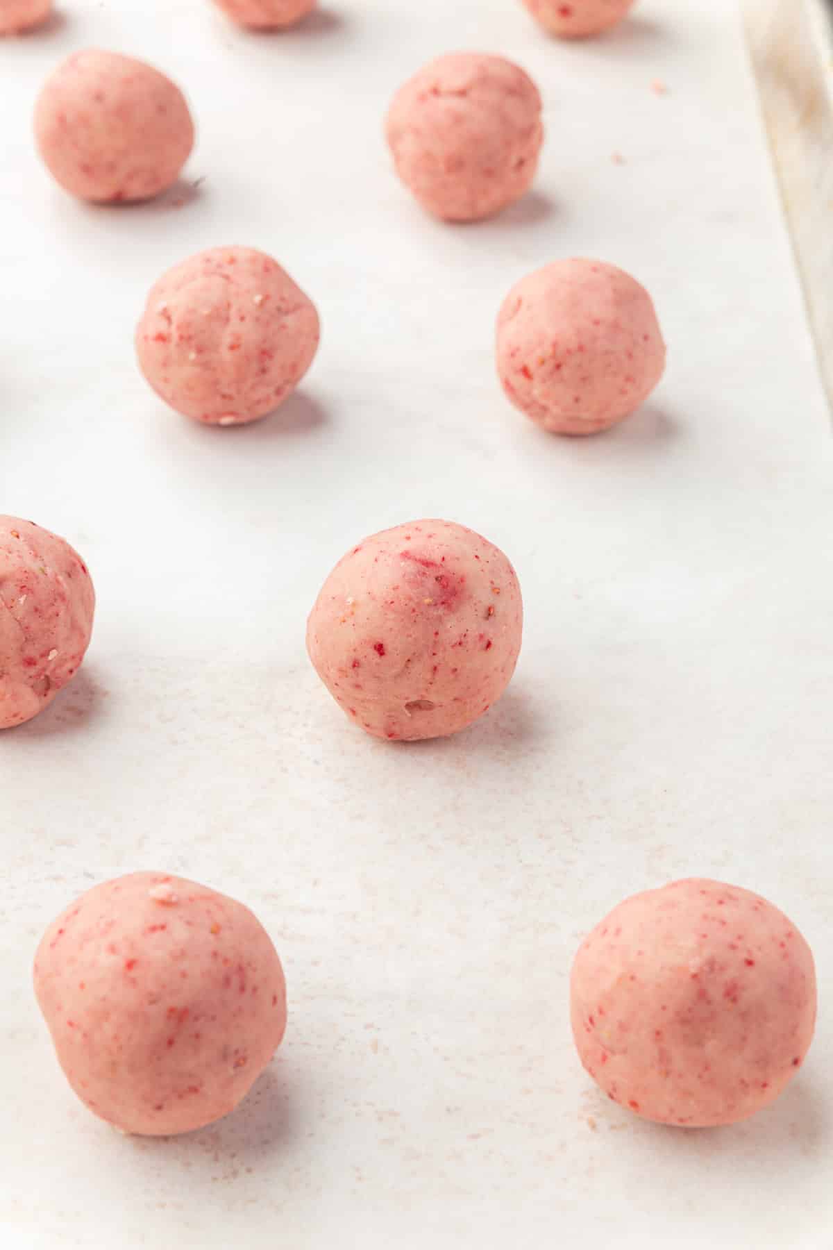A baking sheet lined with parchment paper with a dozen strawberry truffle balls on it.