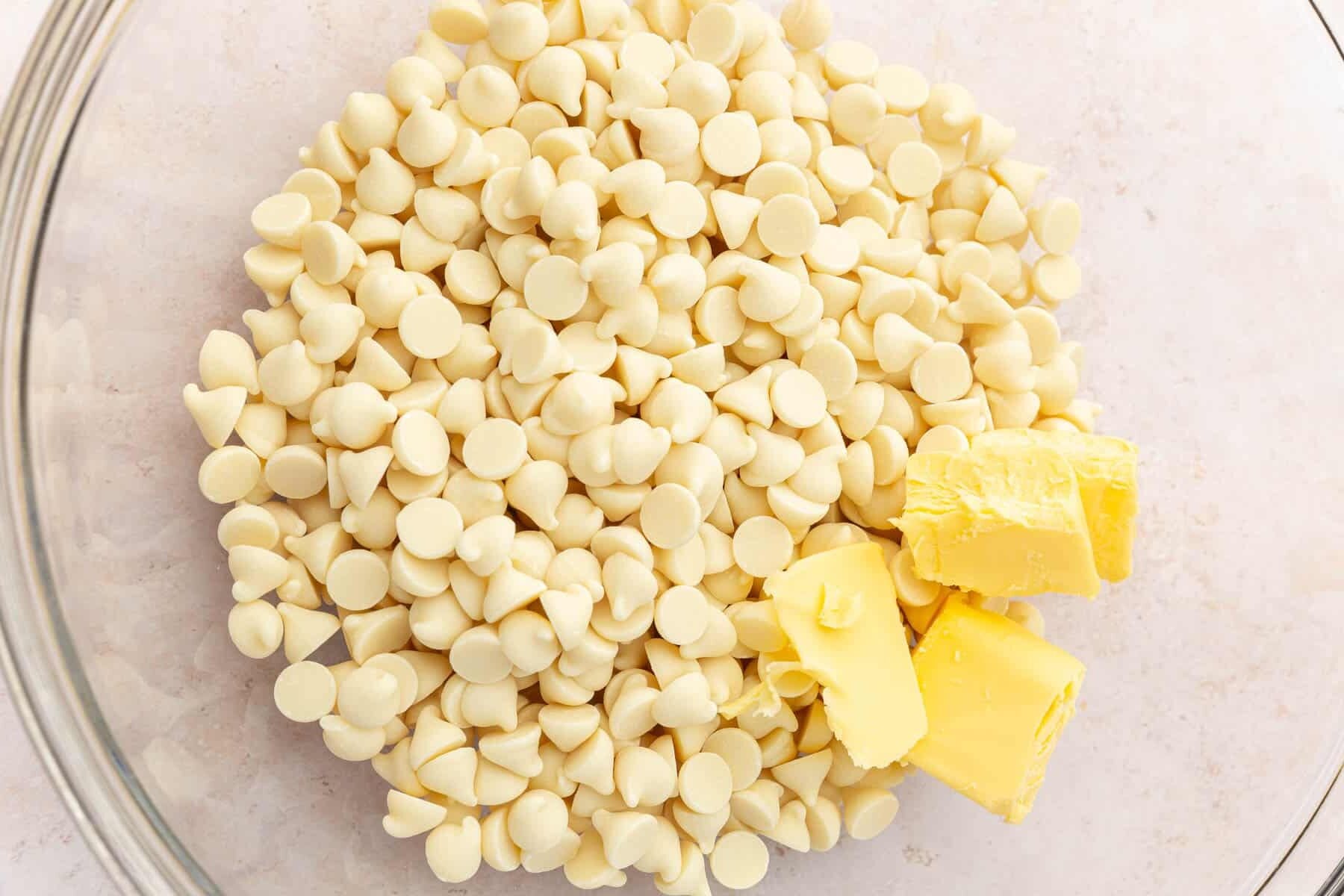 A closeup of a glass bowl with white chocolate chips and butter in it.