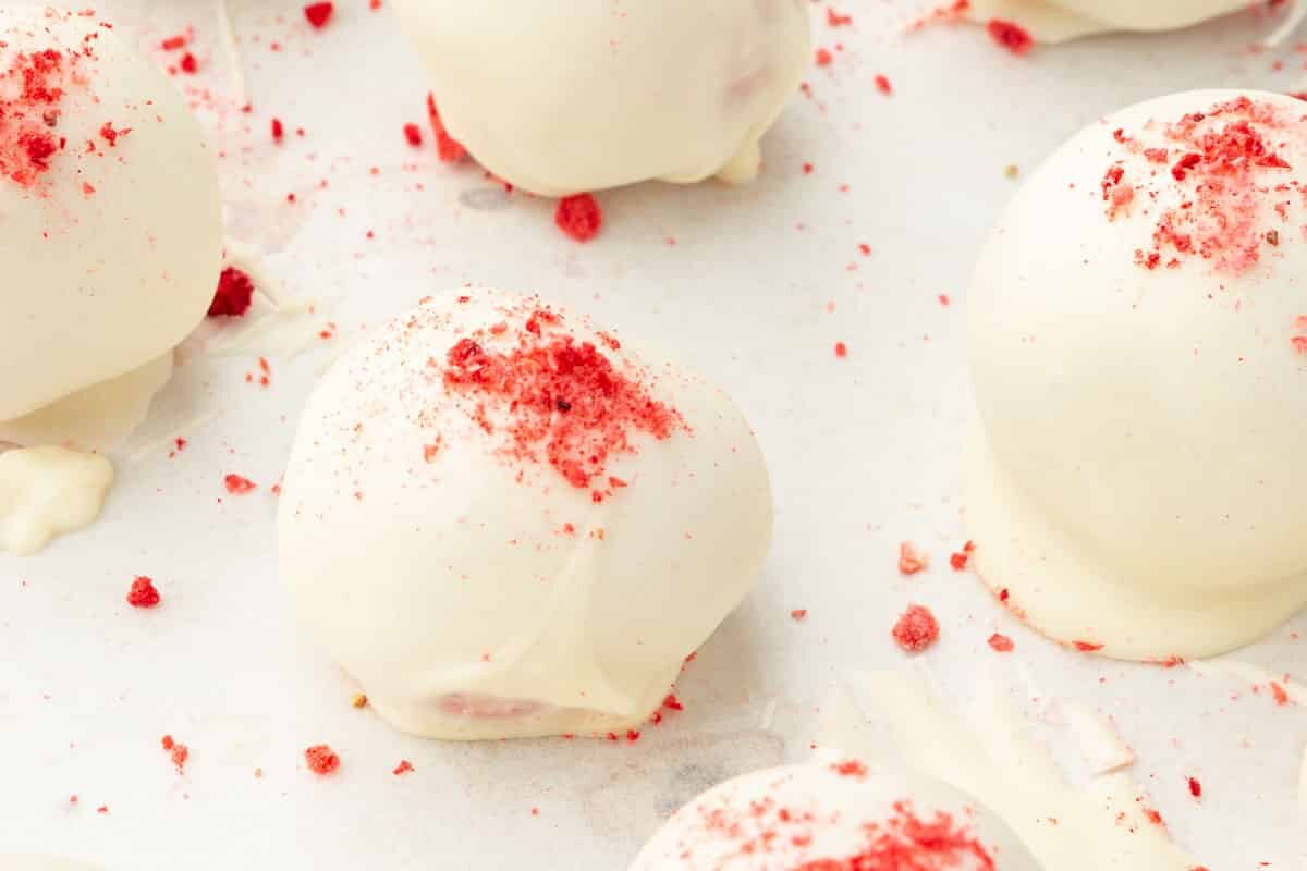 White chocolate truffle balls topped with freeze-dried strawberry powder on parchment paper.