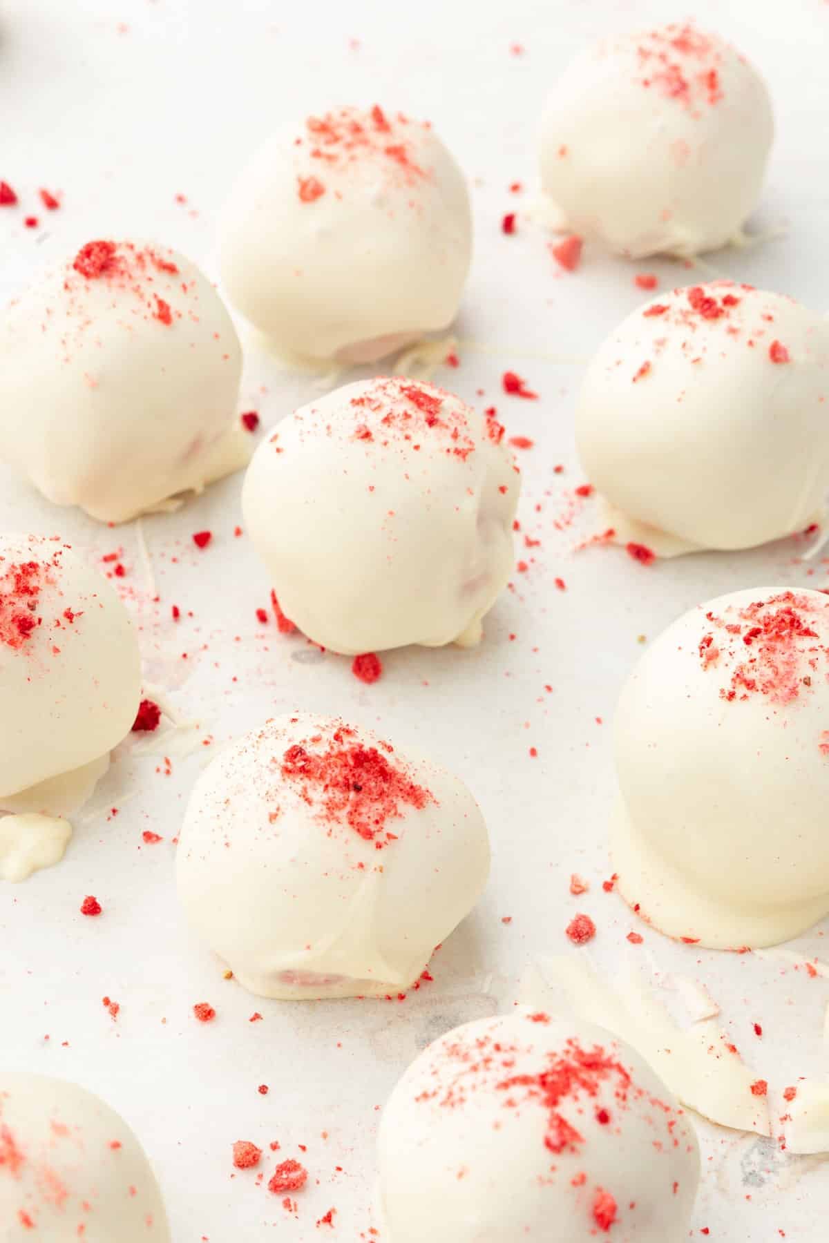 White chocolate truffle balls topped with freeze-dried strawberry powder on parchment paper.