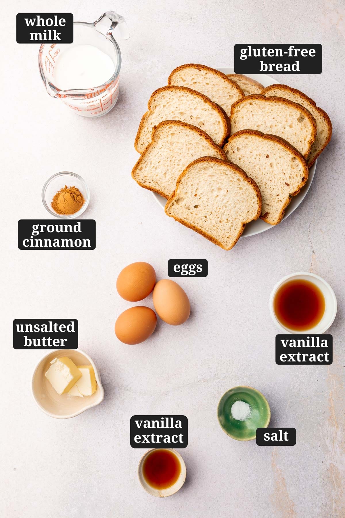 Ingredients in small bowls to make gluten-free french toast, including whole milk, gluten-free bread, ground cinnamon, eggs, vanilla extract, unsalted butter, vanilla extract, and salt with text overlays over each ingredient.