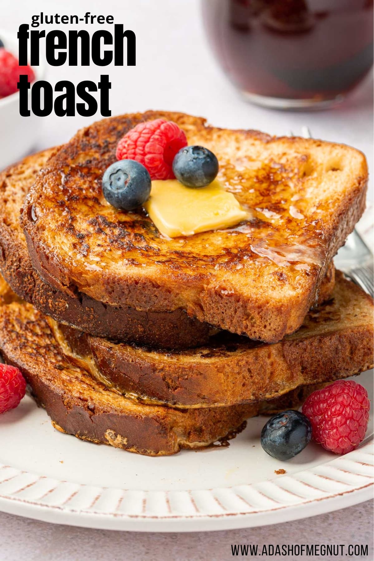 A stack of 4 slices of gluten free french toast topped with butter, syrup, blueberries and raspberries.