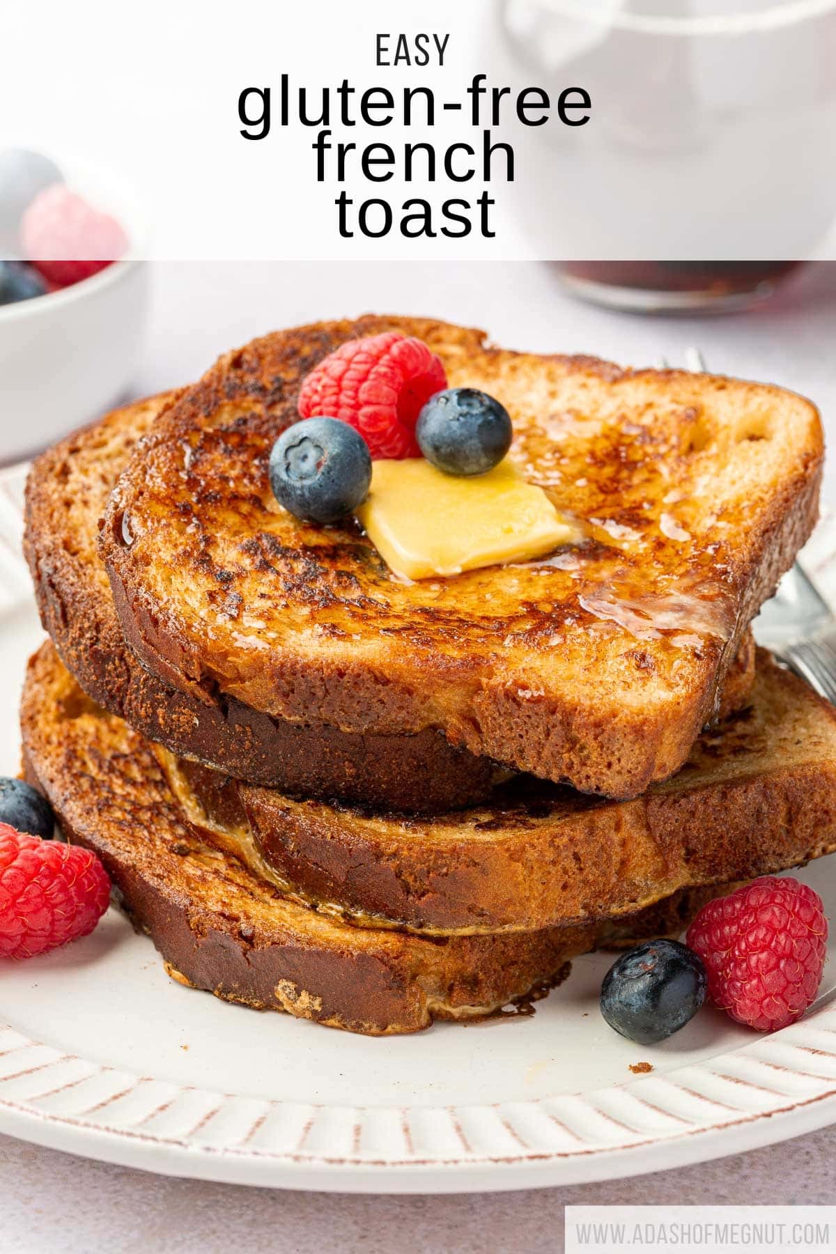 A stack of four slices of gf french toast topped with berries, butter and maple syrup.