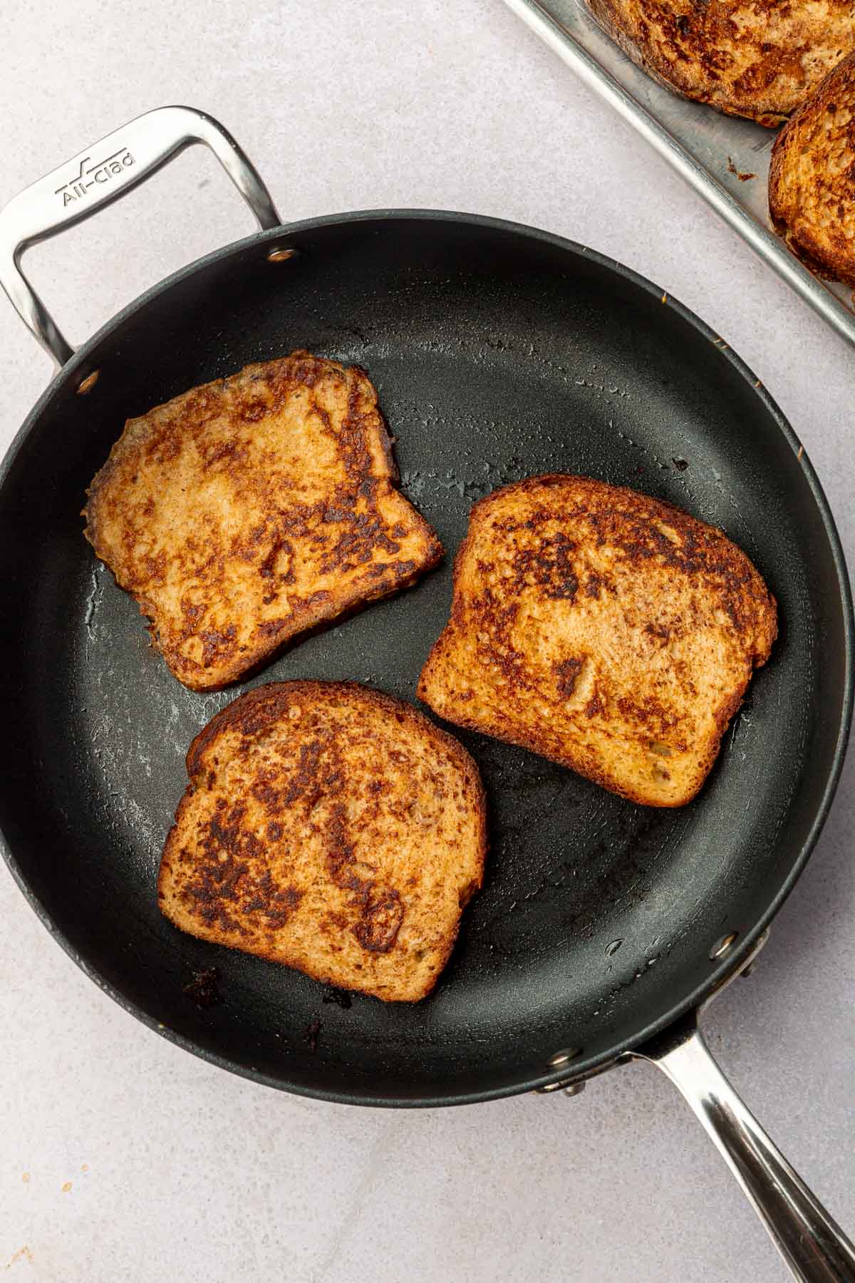 A non-stick skillet with three slices of gluten-free French toast in it.