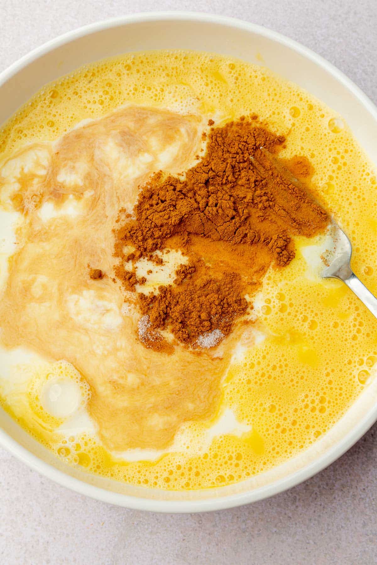A shallow bowl of beaten eggs, milk, vanilla extract, and ground cinnamon.