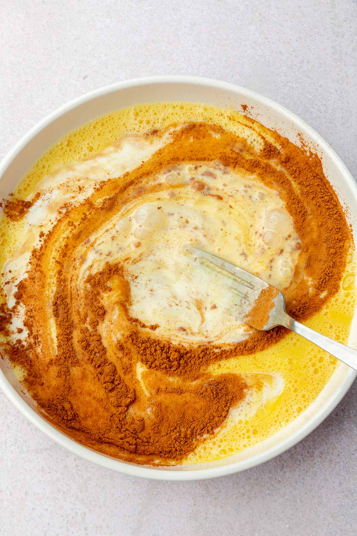 A shallow bowl with a fork mixing together eggs, cinnamon and milk.