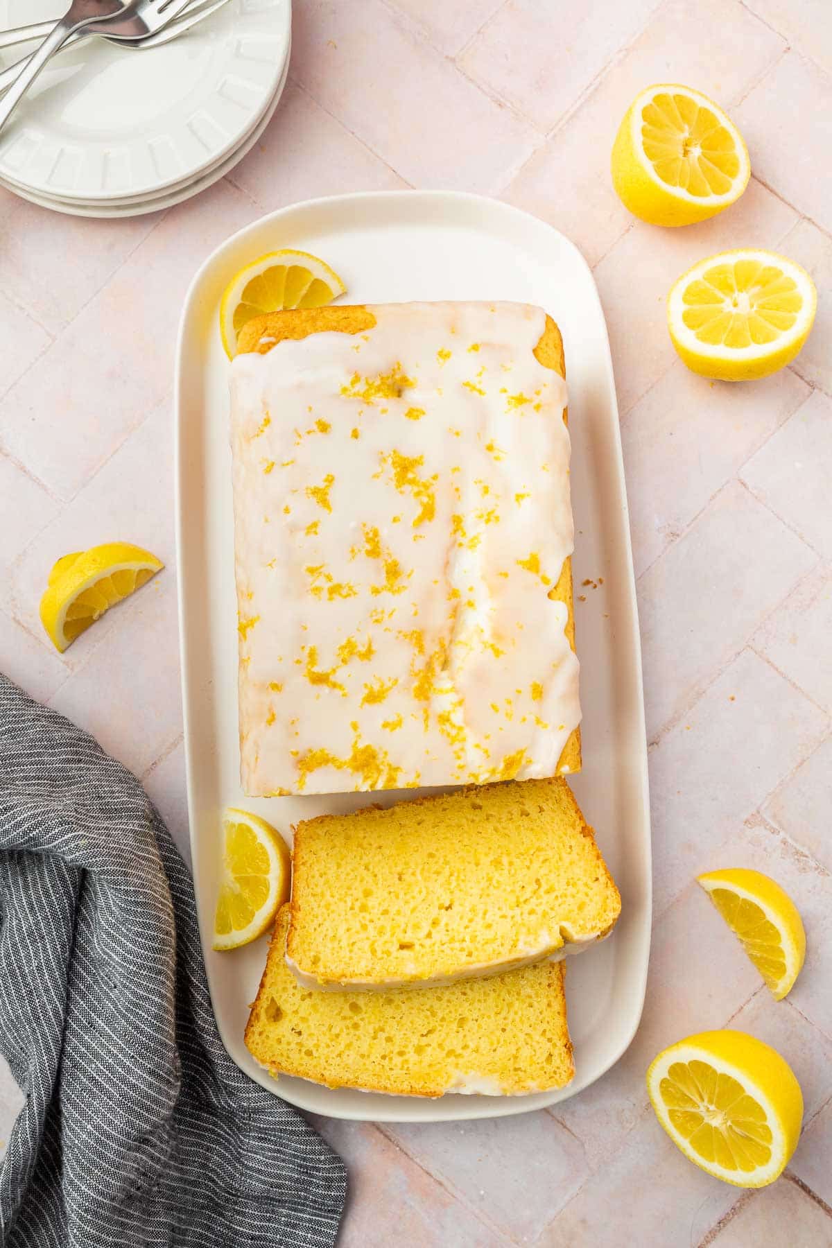 An overhead view of a gluten-free lemon drizzle cake loaf with two slices cut off of it and fresh lemon slices surrounding the cake.