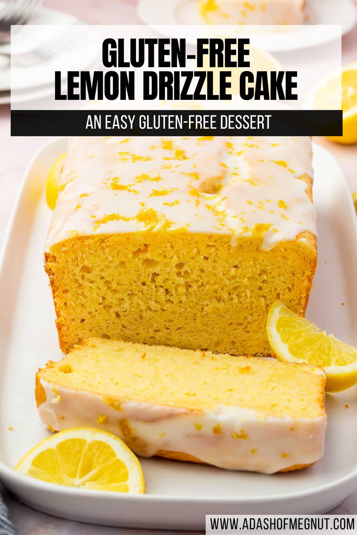 A lemon drizzle cake loaf on a platter with the front slice cut off and lemon wedges surrounding the cake.