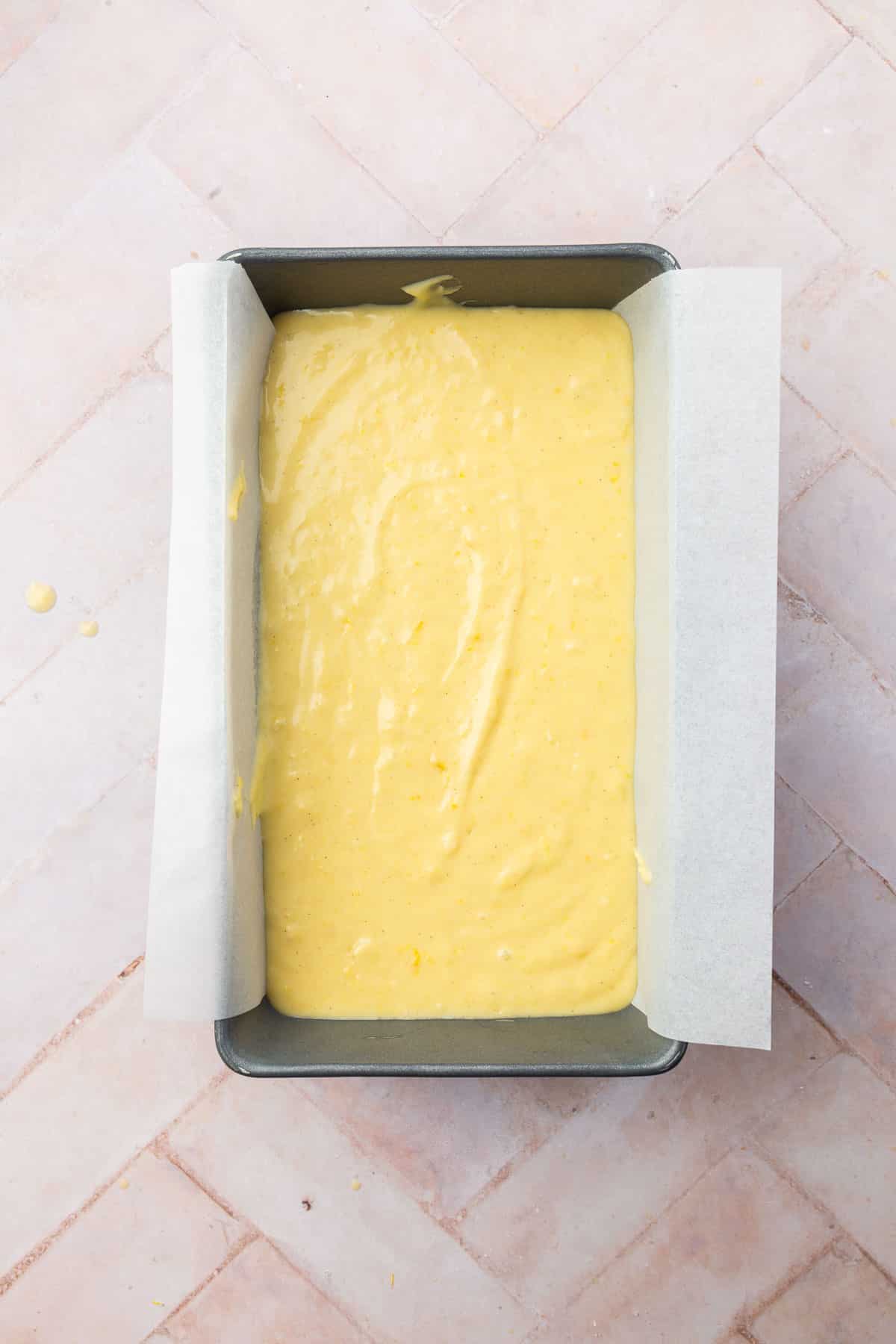 A loaf pan lined with parchment paper with gluten-free lemon drizzle cake batter in it.