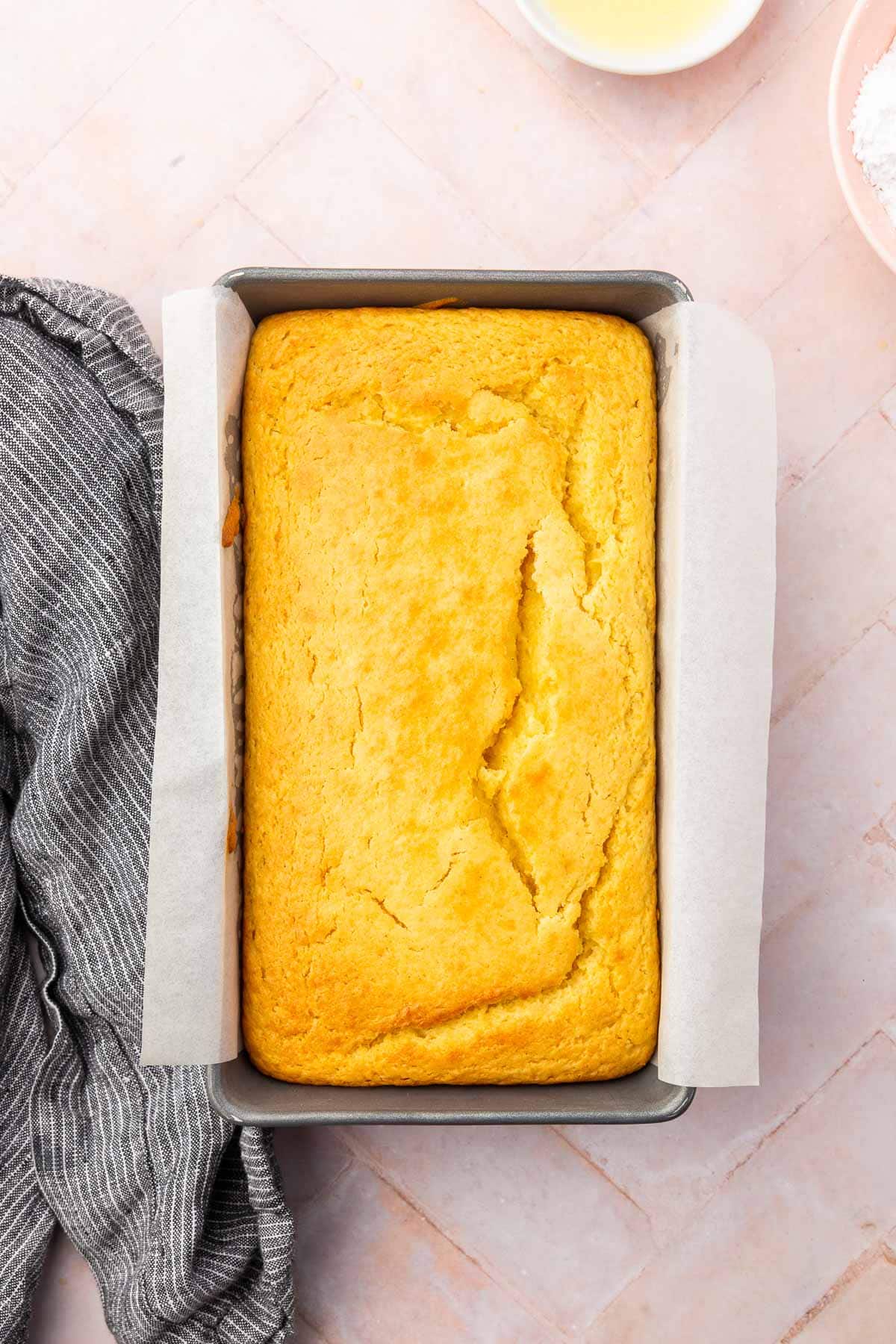 A gluten-free lemon drizzle cake in a loaf pan lined with parchment paper.