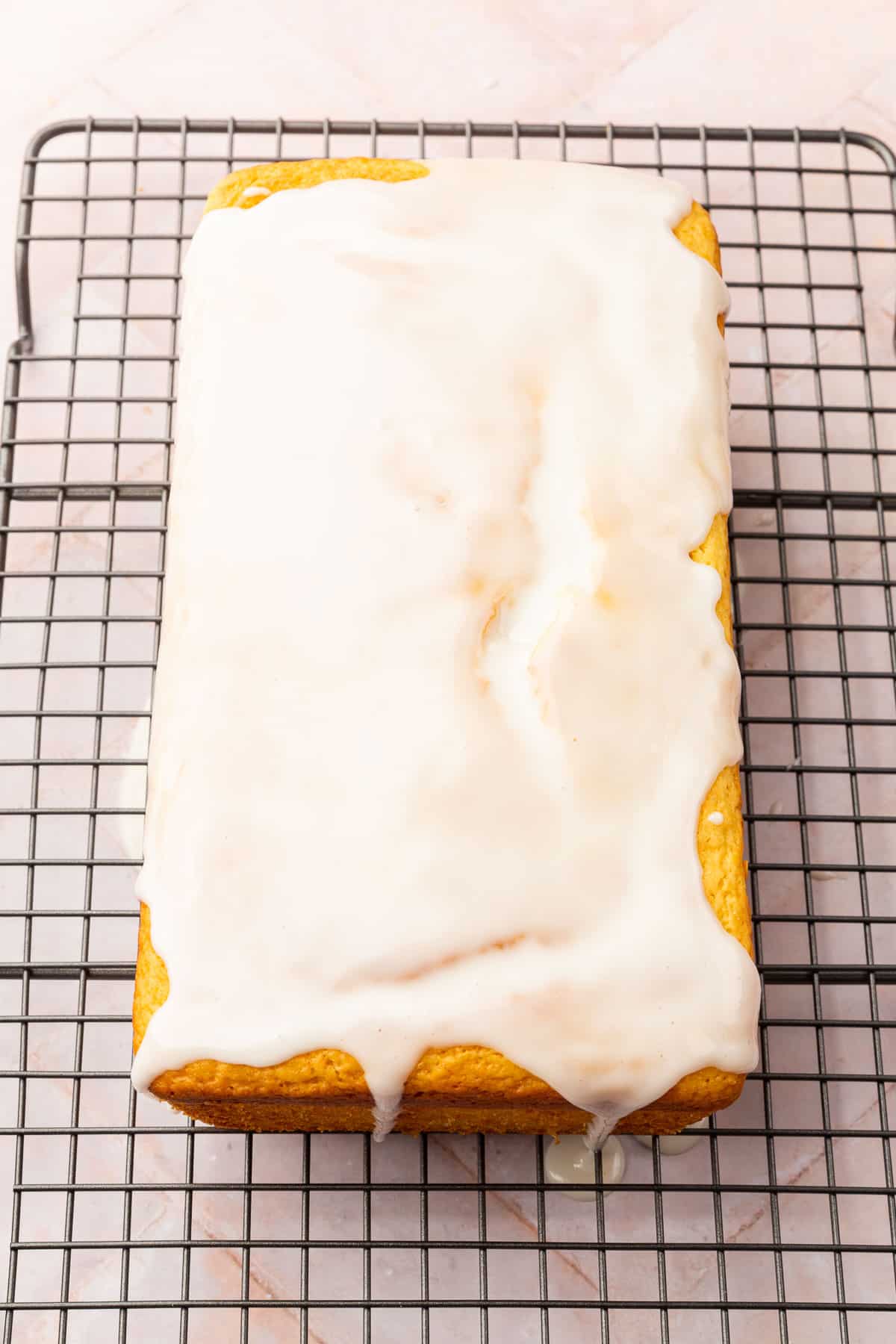 A lemon loaf topped with a white glaze on a cooling rack.