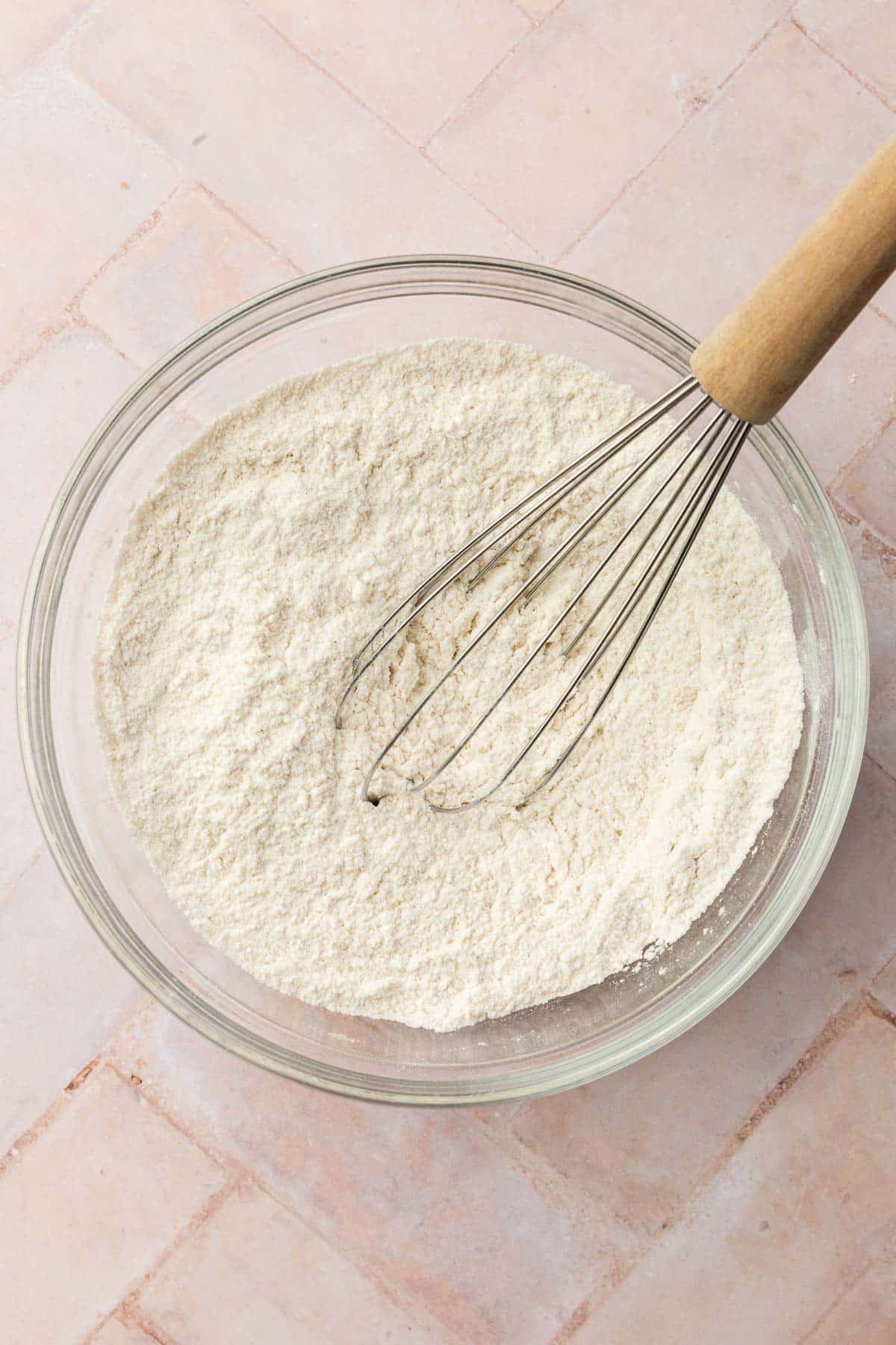 A glass mixing bowl with a gluten-free flour blend in it with a whisk.