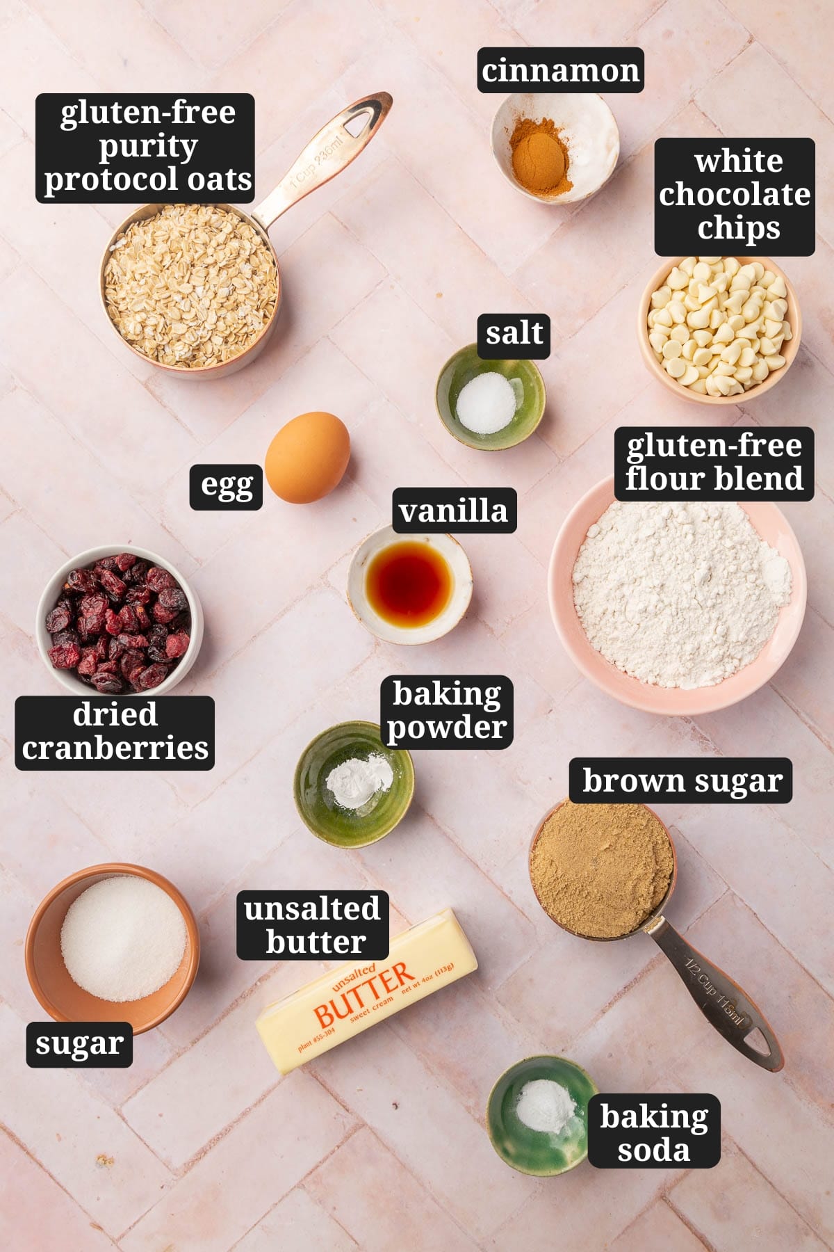 Ingredients in small bowls to make gluten-free oatmeal craisin cookies, including gluten-free oats, cinnamon, salt, white chocolate chips, egg, vanilla, dried cranberries, gluten-free flour, baking powder, granulated sugar, butter, brown sugar and baking soda with text overlays over each ingredient.