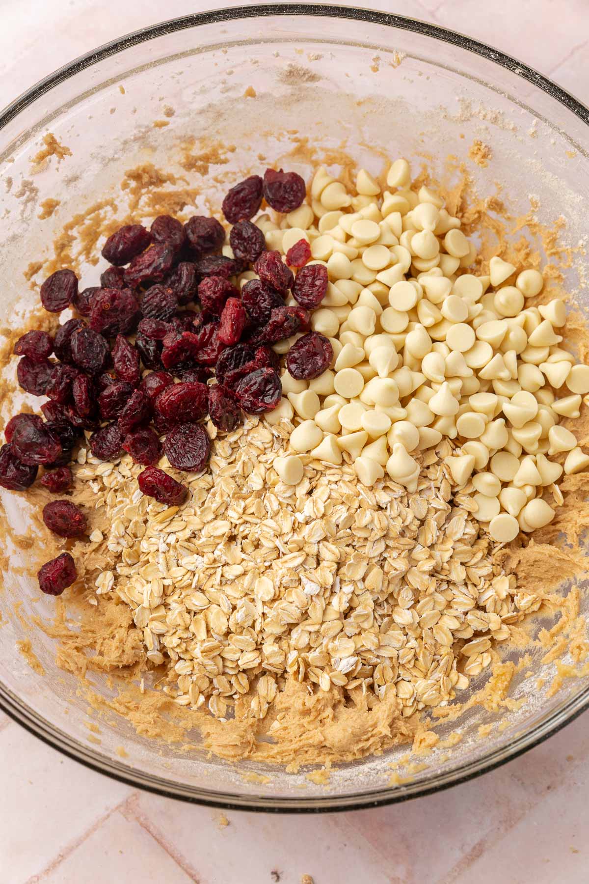 A glass mixing bowl of gluten-free cookie dough topped with dried cranberries, white chocolate chips and gluten-free certified oats.