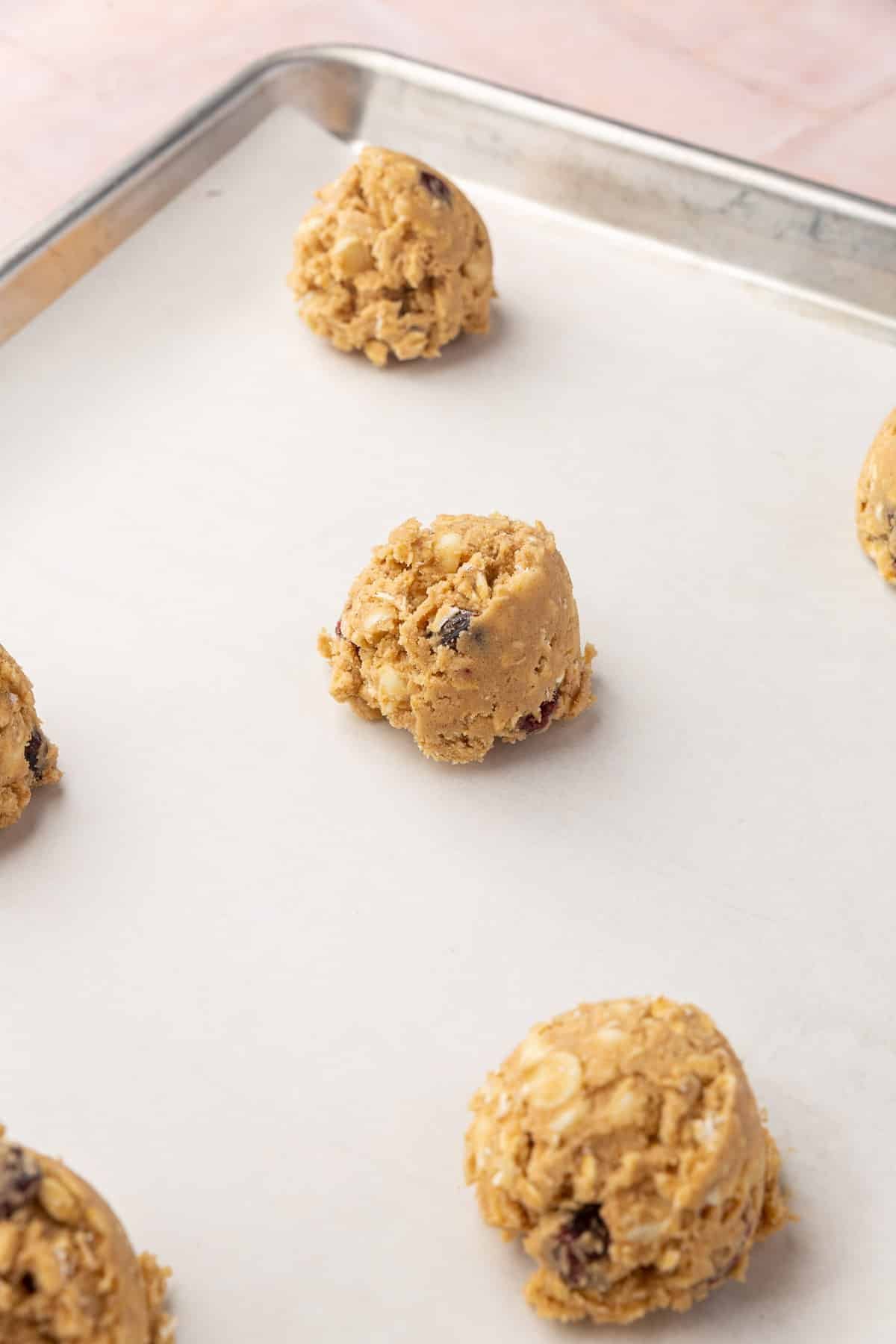 Balls of oatmeal craisin cookie dough on a baking sheet lined with parchment paper.