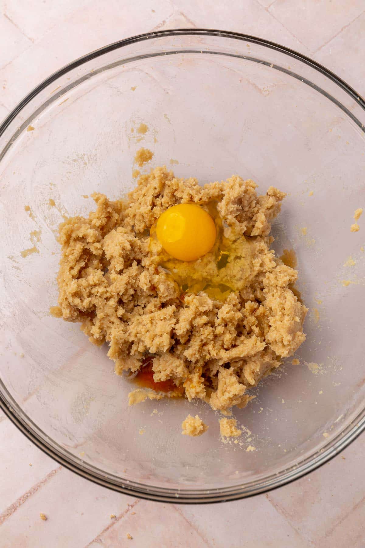 A glass mixing bowl with creamed butter and brown sugar topped with vanilla extract and an egg.