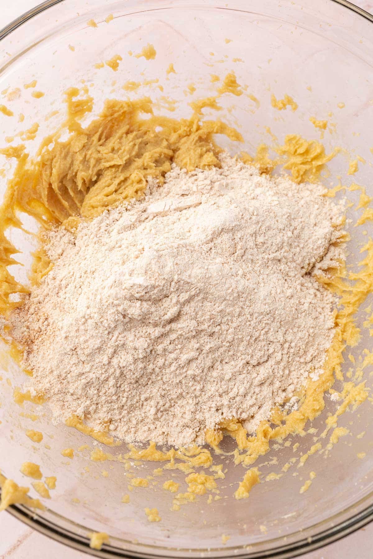 A glass mixing bowl of gluten-free batter topped with gluten-free flour blend.