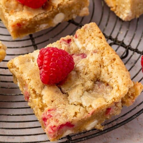 A single raspberry white chocolate blondie topped with fresh raspberries on a round cooling rack.