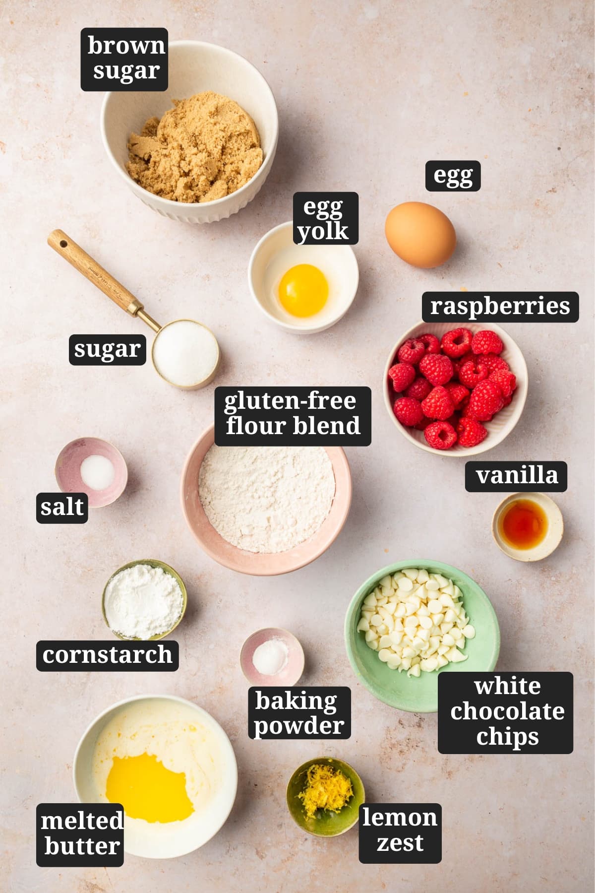 Ingredients in small bowls to make gluten free white chocolate raspberry blondies, including brown sugar, egg yolk, egg, sugar, raspberries, gluten-free flour blend, salt, cornstarch, baking powder, white chocolate chips, vanilla, lemon zest, and melted butter with text overlays over each ingredient.