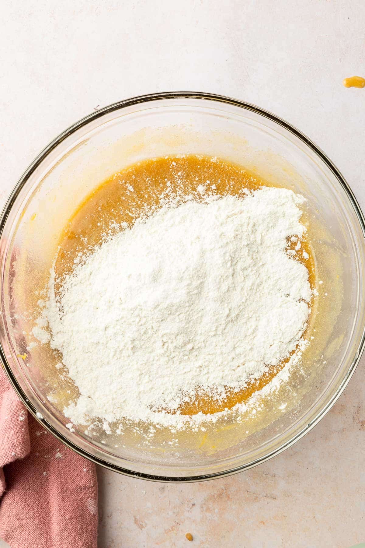 A glass mixing bowl with gluten-free flour topped on a golden mixture.