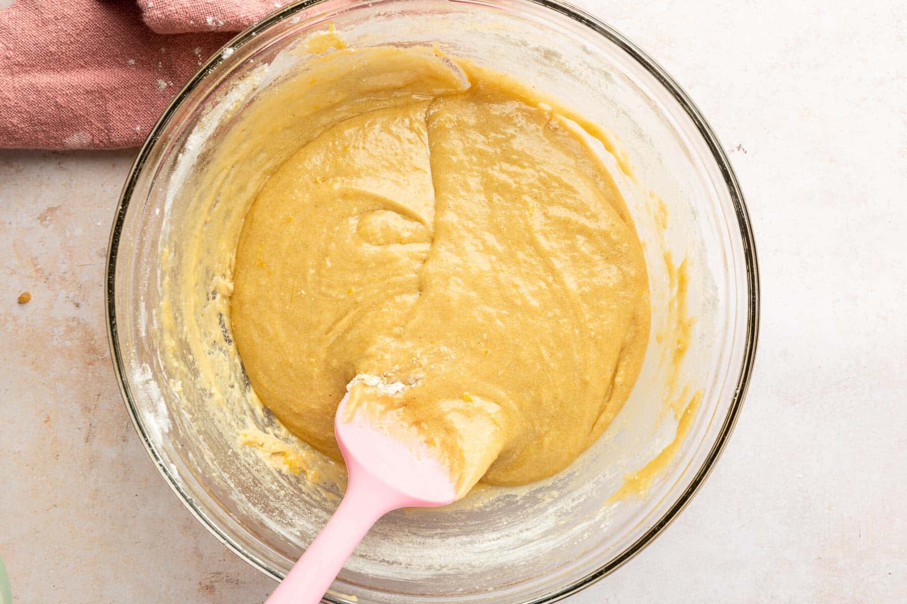 A glass mixing bowl with gluten-free blondie batter in it with a pink rubber spatula.