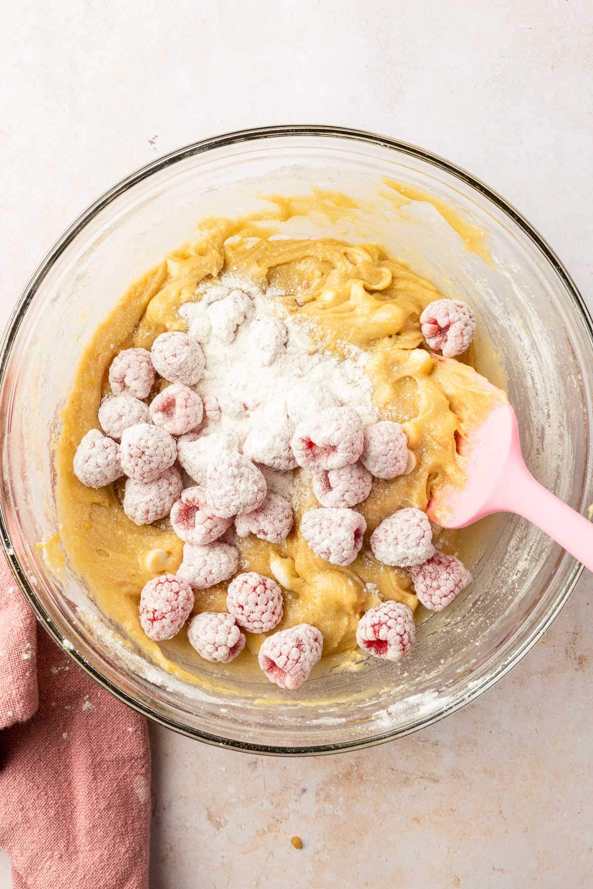 A glass mixing bowl with a gluten-free blondie batter topped with gluten-free flour and fresh raspberries.