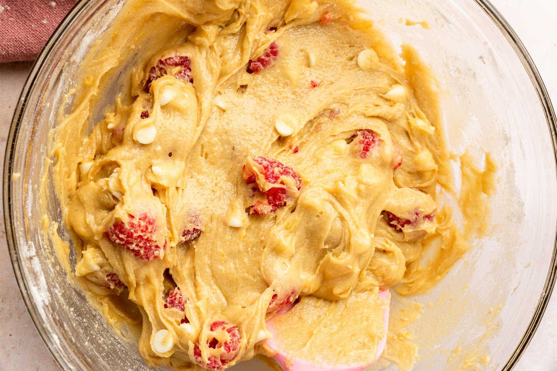 A glass mixing bowl of gluten free white chocolate raspberry blondie batter in it.