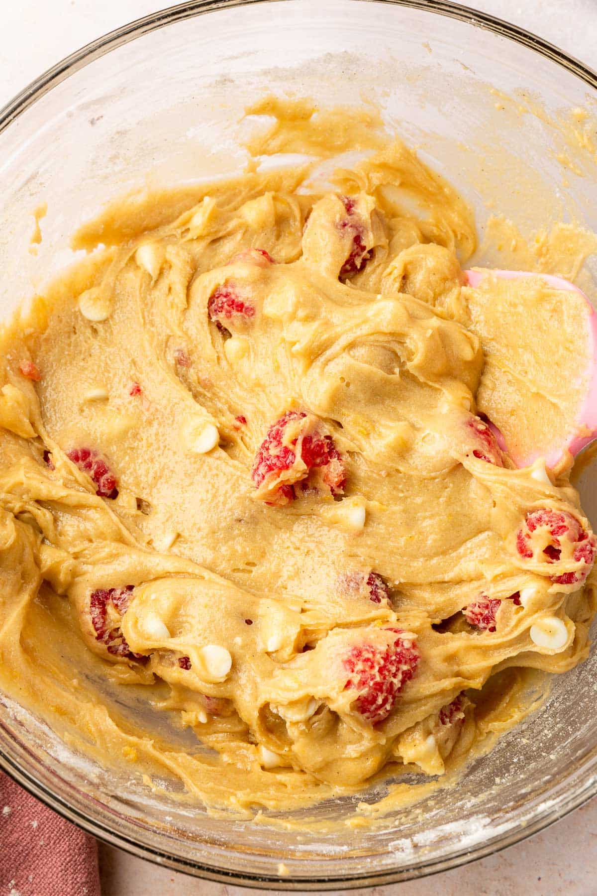 A glass mixing bowl of gluten free white chocolate raspberry blondie batter in it.