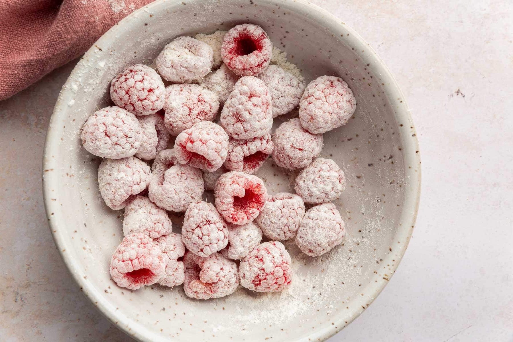 A ceramic bowl with fresh raspberries covered in gluten-free flour in it.