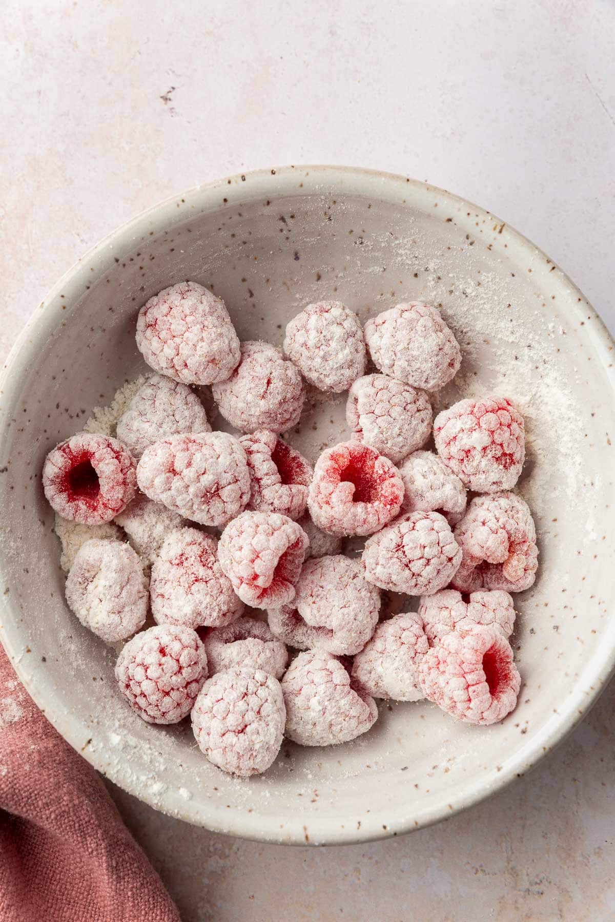 A ceramic bowl with fresh raspberries covered in gluten-free flour in it.