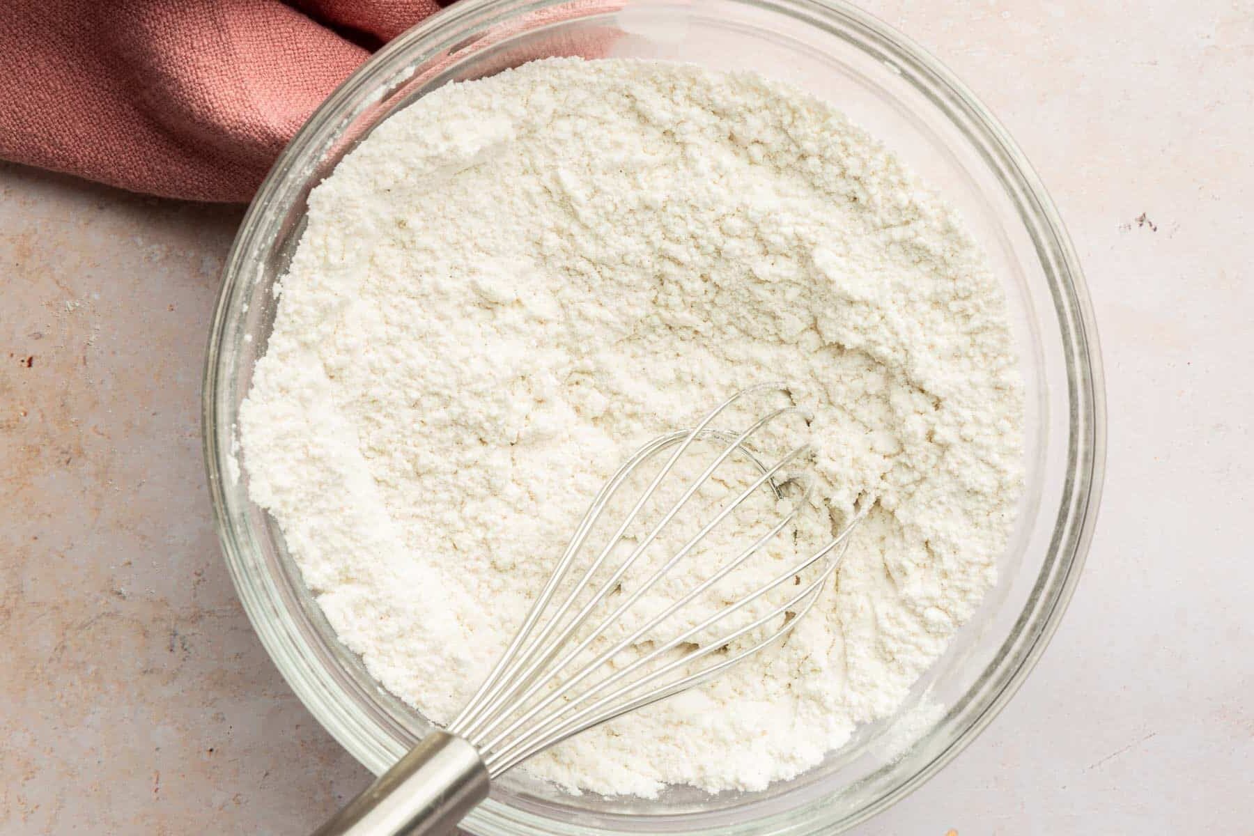 A glass mixing bowl with a gluten-free flour mixture and a whisk.