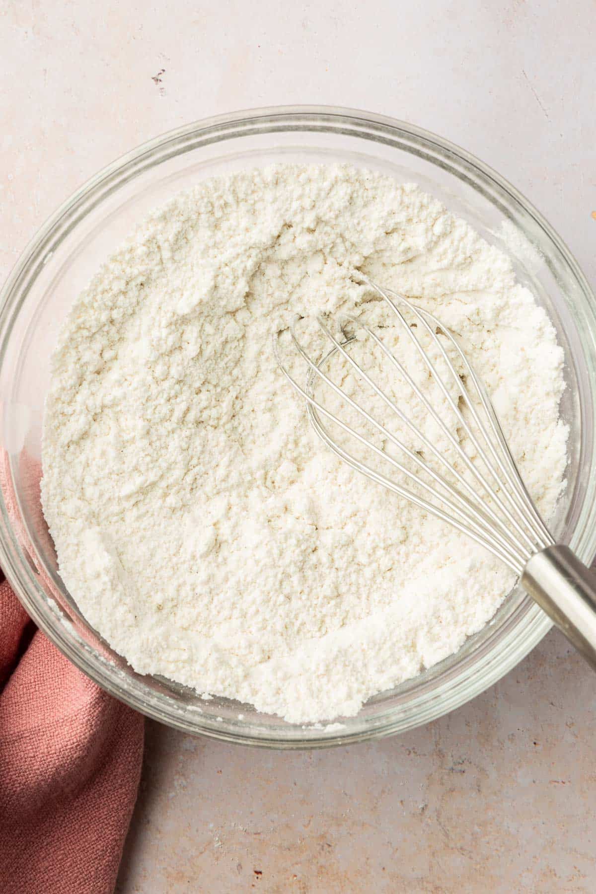 A glass mixing bowl with a gluten-free flour mixture and a whisk.