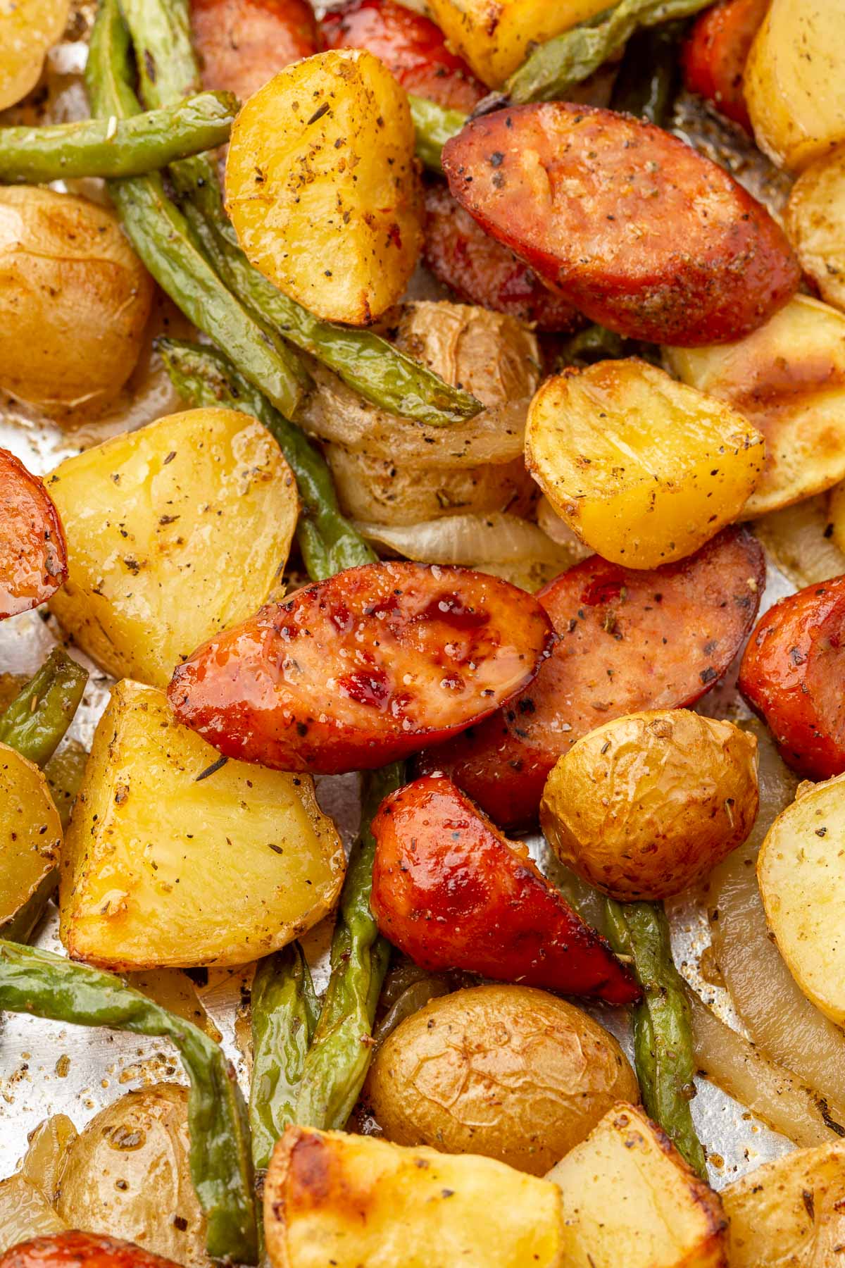 A close up of roasted sausage, potatoes and green beans on a sheet pan.