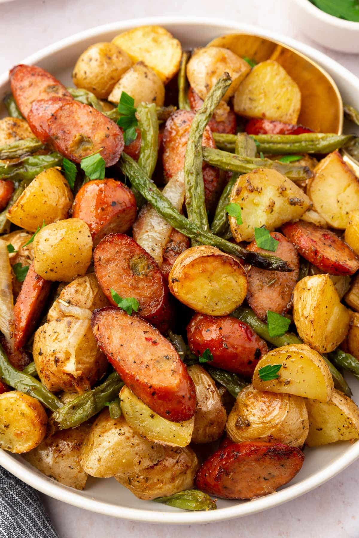 Roasted sausage, green beans, onions, and potatoes in a serving bowl.