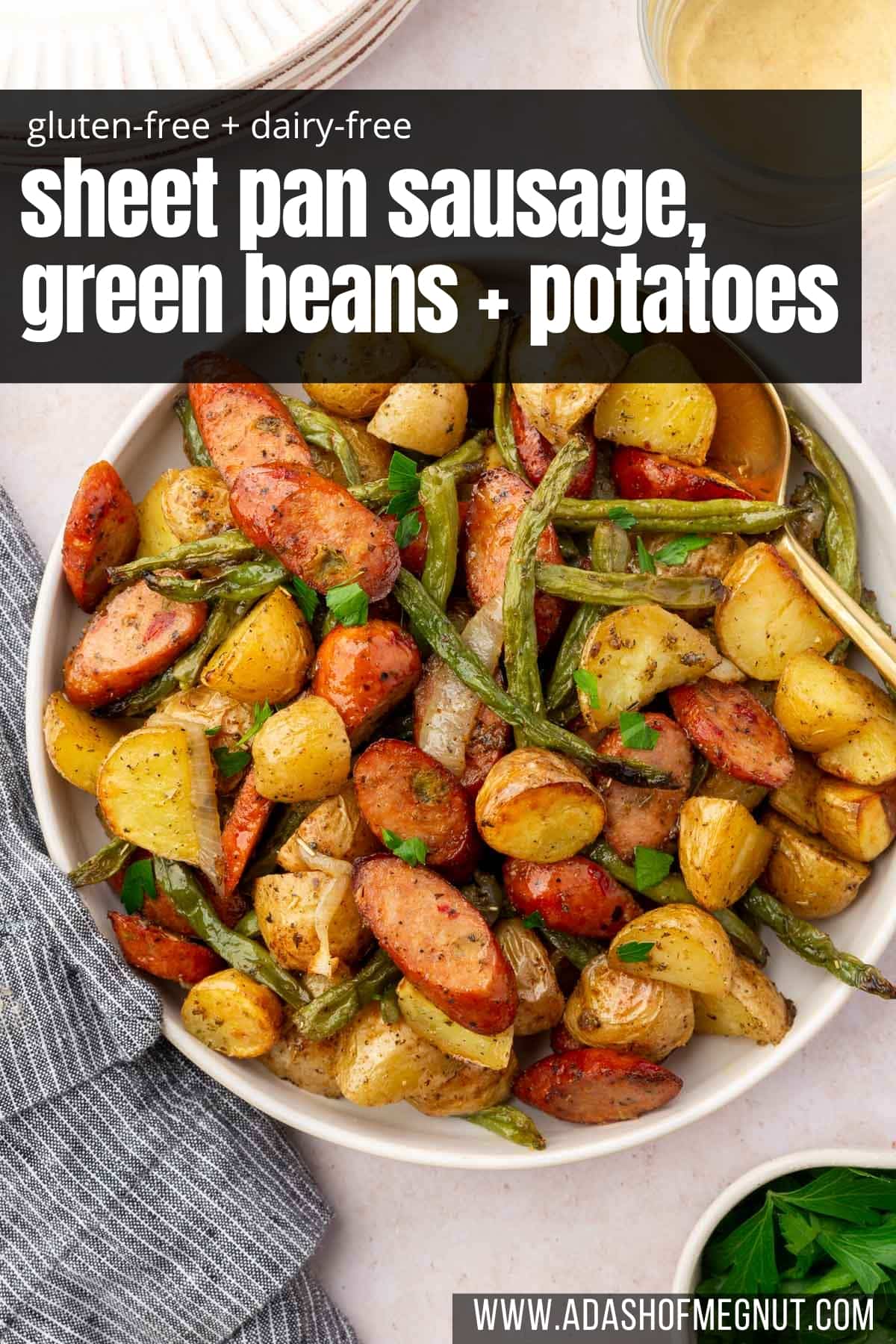 An overhead view of a serving bowl with roasted andouille sausage, green beans, and baby potatoes with fresh parsley.