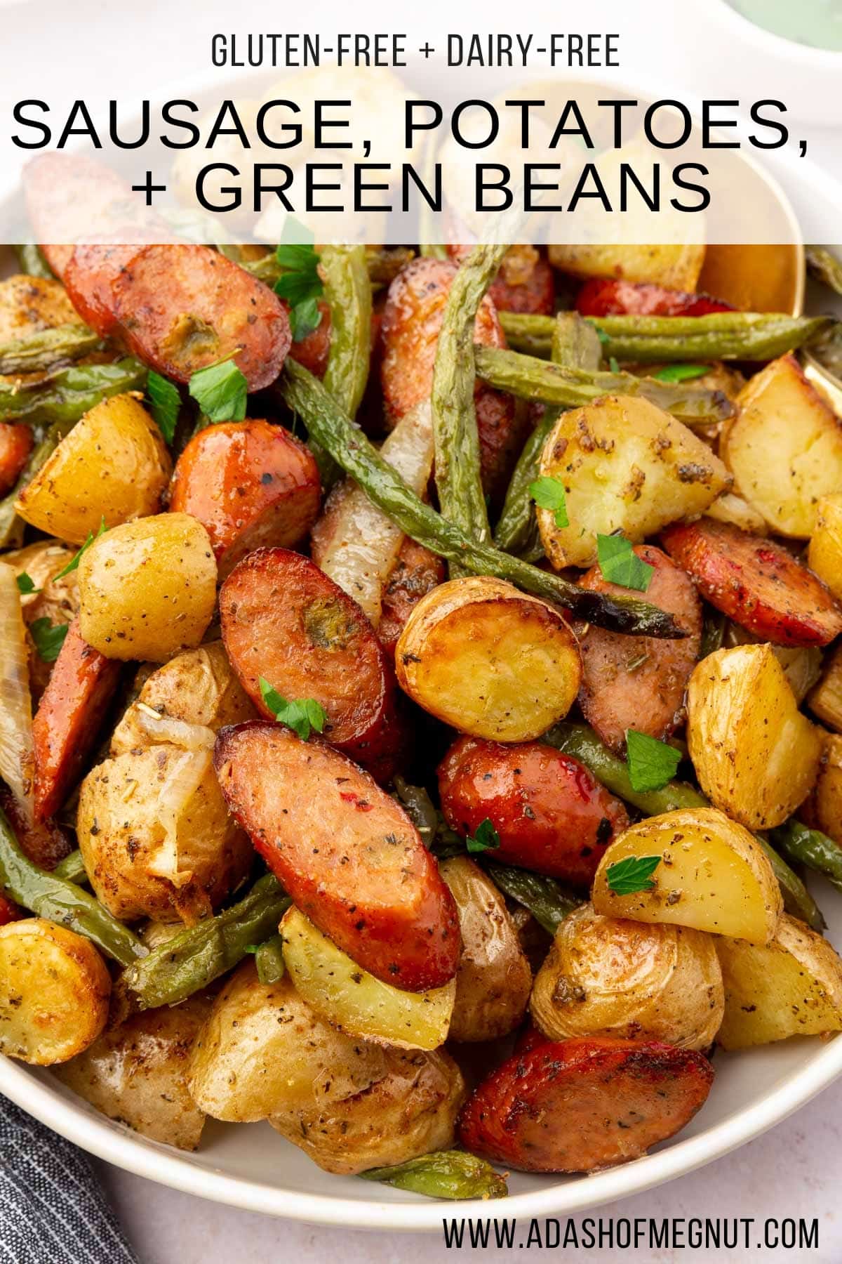 A serving bowl of roasted potatoes, green beans, and sausage topped with parsley.
